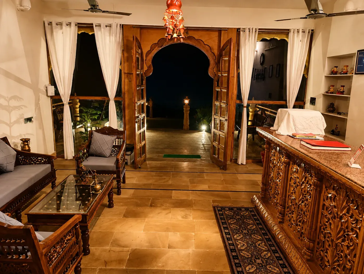 Warmly lit reception lounge with carved teak desk, arched doorway and comfortable seating